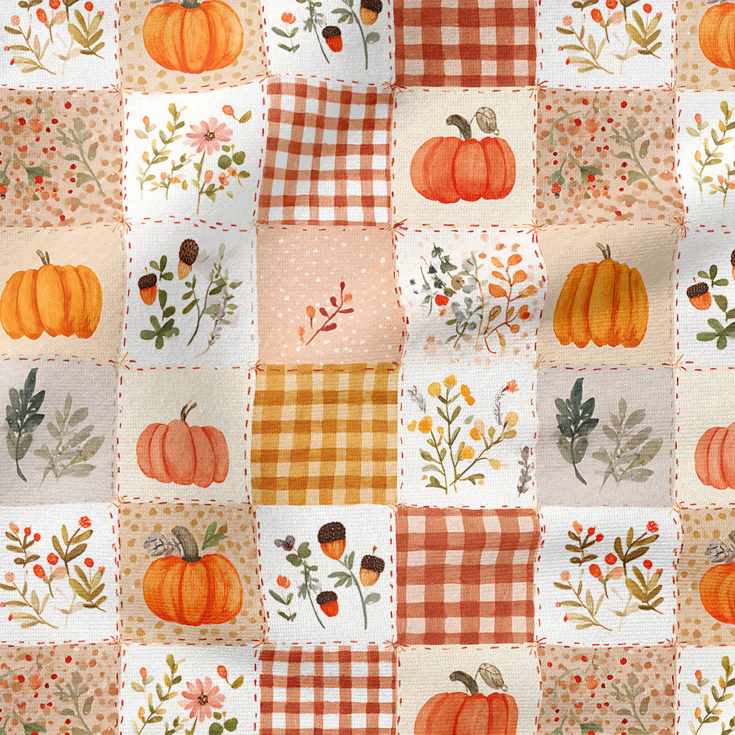 A close-up of an autumn-themed patchwork fabric featuring squares with orange pumpkins, floral prints, gingham checks, and solid warm-toned backgrounds.
