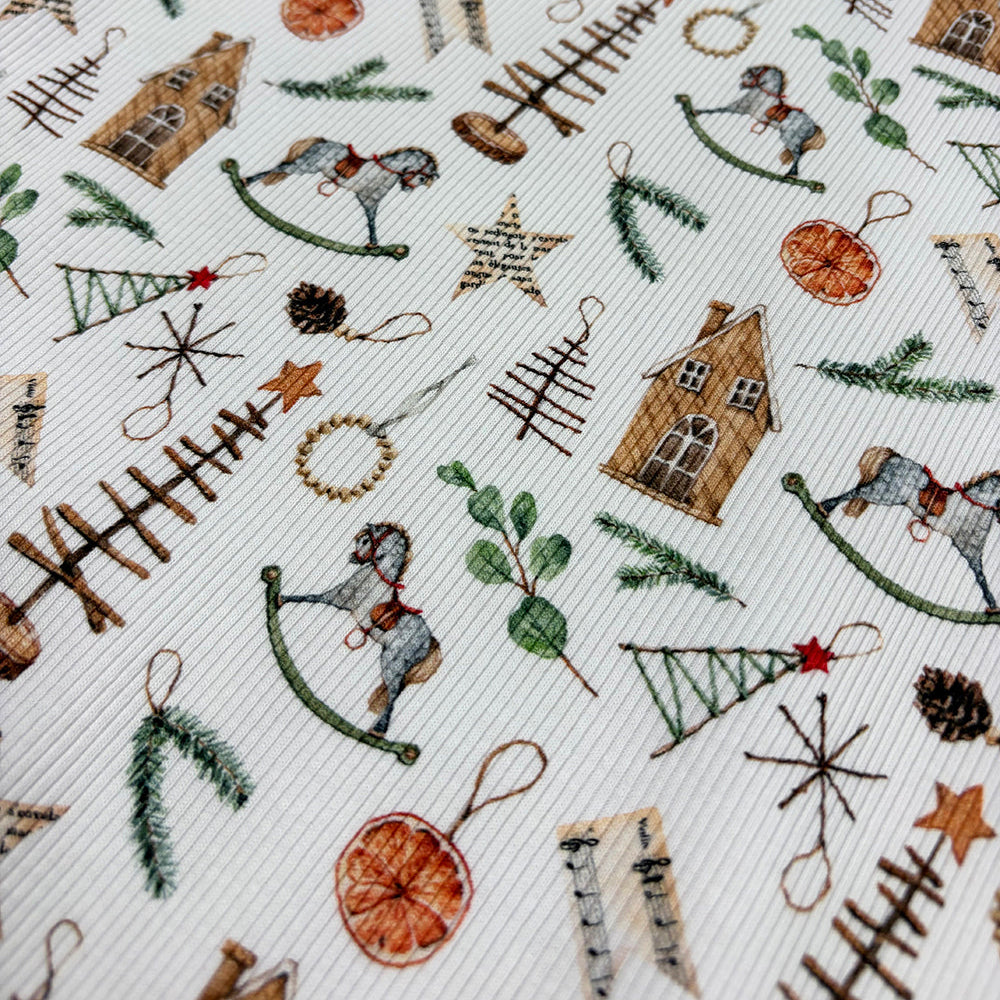A close-up of a white fabric with a detailed Christmas-themed pattern featuring miniature houses, rocking horses, pine trees, stars, pinecones, and evergreen branches.
