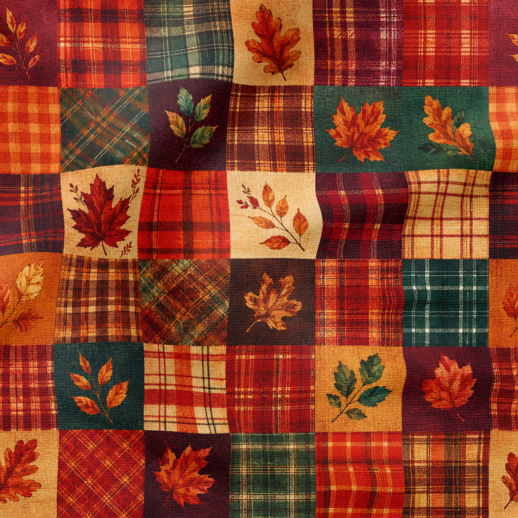 Autumn-themed fabric with a patchwork design featuring red, orange, and green plaid squares, interspersed with panels showing embroidered or printed maple leaves and leafy branches.