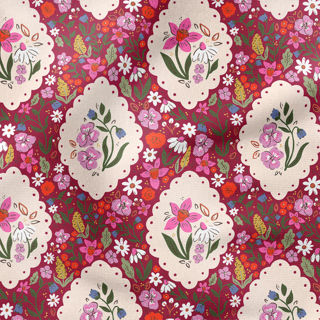 A close-up of a floral fabric pattern featuring cream-colored scalloped oval medallions with pink flowers and green leaves, set against a dark red background filled with smaller multicolored blossoms.