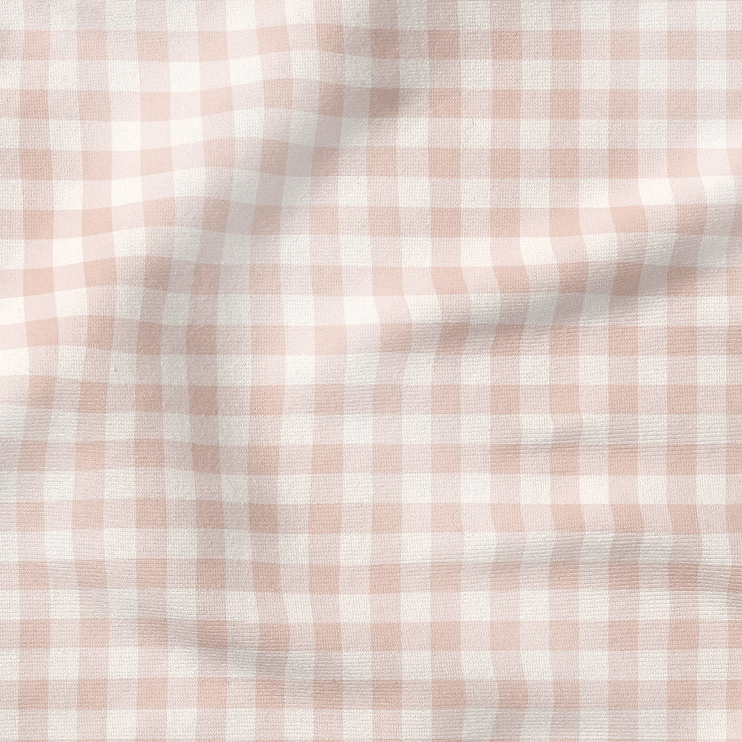 A close-up of a soft, draped fabric with a light pink and white gingham checkered pattern.