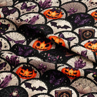 A close-up of a Halloween-themed fabric featuring a repeating pattern of black cats, purple butterflies, orange jack-o'-lanterns, bats, skulls, and spiderwebs on a black and off-white background.
