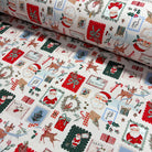 A close-up of a rolled piece of Christmas-themed fabric laid over an unrolled section of the same fabric. The off-white woven background is covered in festive patchwork motifs including Santa Claus, reindeer, candy canes, wreaths, stockings, and red gift boxes.