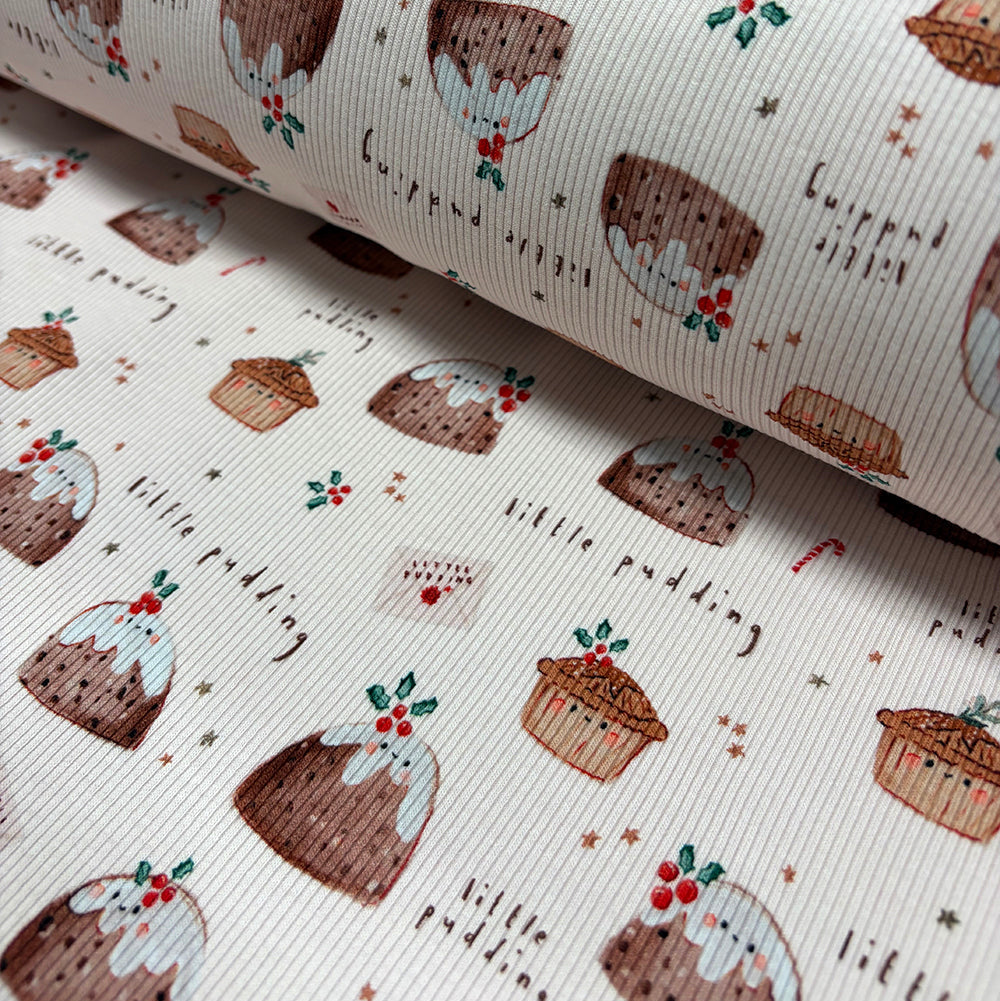 A close-up of a ribbed fabric or wallpaper with a repeating pattern of Christmas puddings, text reading 'little pudding', and small festive illustrations on an off-white background.