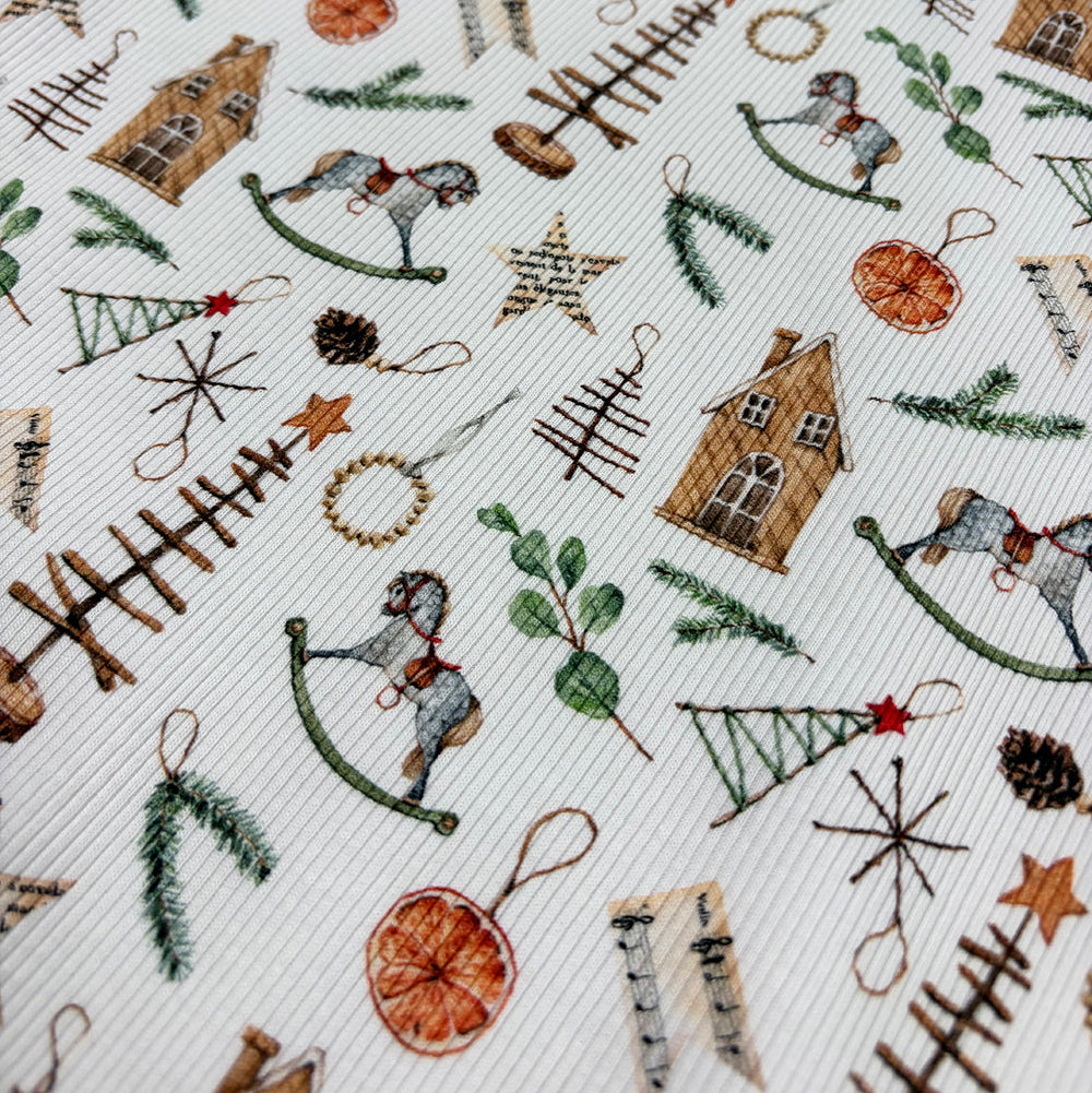 A close-up of a white fabric with a detailed Christmas-themed pattern featuring miniature houses, rocking horses, pine trees, stars, pinecones, and evergreen branches.