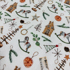 A close-up of a white fabric with a detailed Christmas-themed pattern featuring miniature houses, rocking horses, pine trees, stars, pinecones, and evergreen branches.