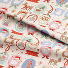 A close-up of festive Christmas-themed fabric with a cream background and a repeating pattern of Santa Claus, reindeer, ornaments, candy canes, and red 'NOEL' banners, with one corner folded over.