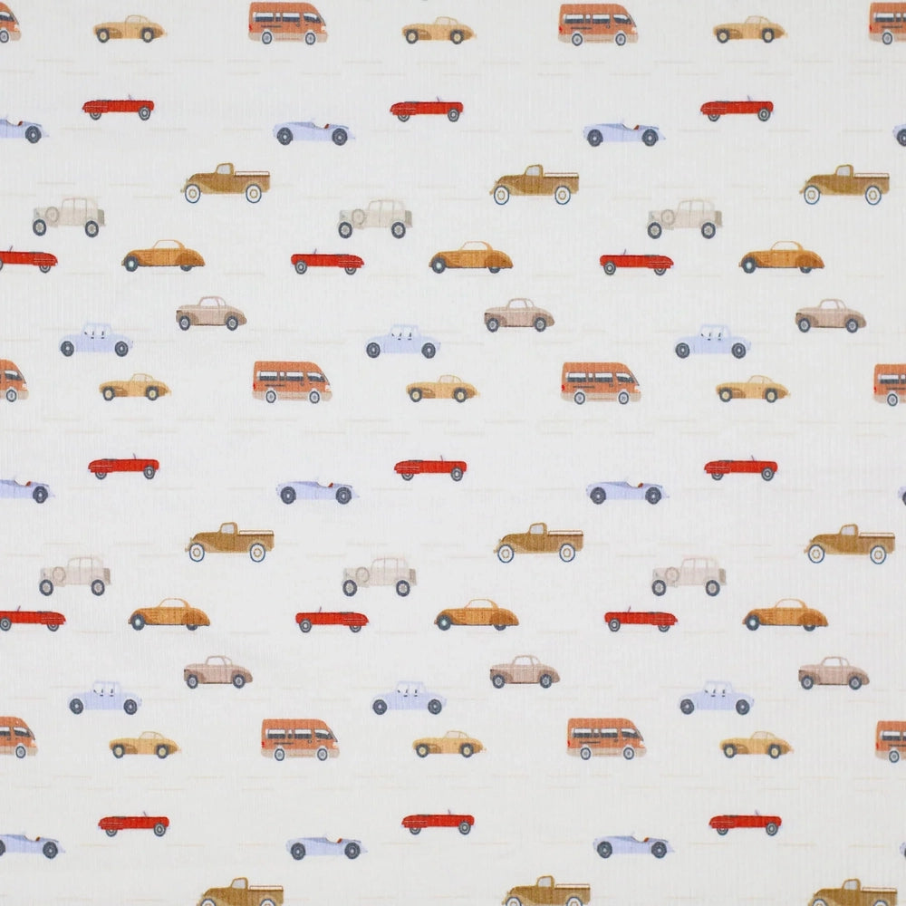 Close-up of white fabric with small, multicolored vehicle illustrations, perfect for kids' apparel and accessories