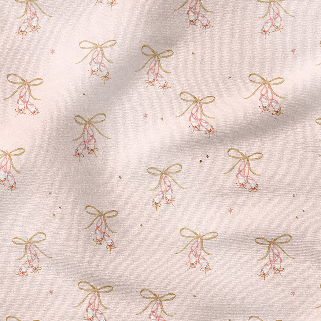 A close-up of a light blush pink fabric with a repeating pattern of small gold bows, pink berries, and tiny gold stars.