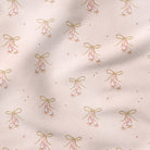 A close-up of a light blush pink fabric with a repeating pattern of small gold bows, pink berries, and tiny gold stars.