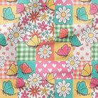 A close-up of a colorful patchwork fabric pattern featuring white daisies, pink and teal butterflies, floral motifs, hearts, gingham checks, and solid pastel blocks.