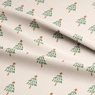 A close-up of a cream-colored fabric with a repeating pattern of small green Christmas trees with orange star toppers, draped with soft folds.