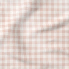 A close-up of a soft, draped fabric with a light pink and white gingham checkered pattern.