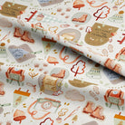 A close-up of a rolled piece of fabric with a whimsical autumn-themed pattern featuring hiking boots, trees, clouds, and small illustrations on an off-white background.