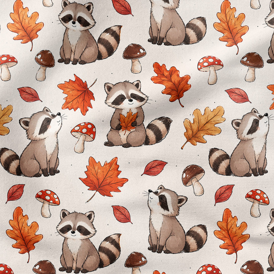 A repeating pattern of watercolor-style raccoons, autumn leaves, and mushrooms on an off-white fabric background. The raccoons are gray and black, surrounded by orange, red, and brown leaves, red-and-white mushrooms, and small brown mushrooms.