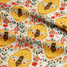A close-up of patterned fabric with a repeating design of yellow bees, red and orange flowers, green leaves, and small blue accents on a white background.