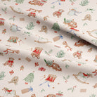 A close-up of a fabric with a festive Christmas pattern featuring teddy bears, rocking horses, sleighs, snowman, Christmas trees, and gifts on an off-white background.