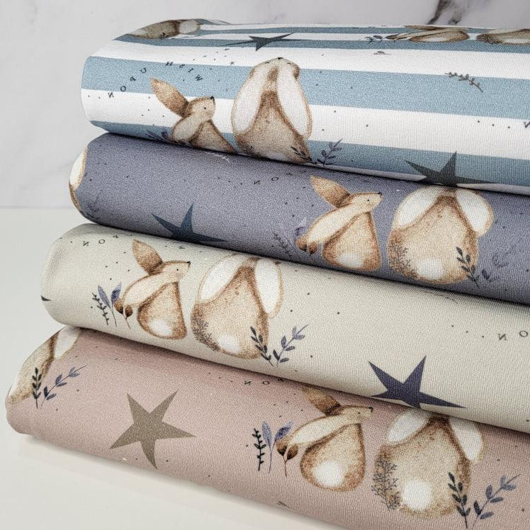 Stack of fabric pieces with a bunny and floral pattern, in various colors including blue, beige, and pink.